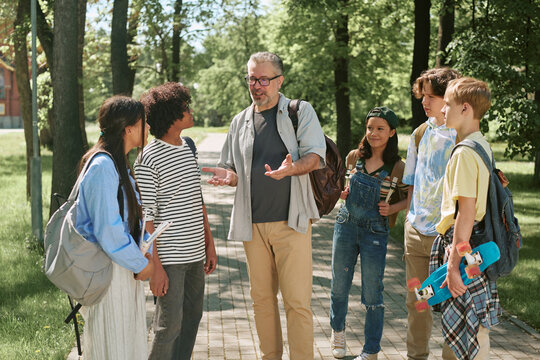 Diverse teenager students gathering with middle aged male teacher, discussing schoolwork outdoors and supporting teamwork. Ideal for education marketing, mentoring, youth learning