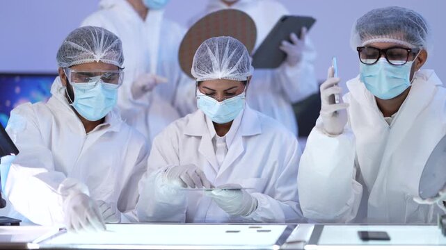 A team of scientists in coveralls inspect wafer discs on an illuminated inspection table in a high-tech cleanroom.