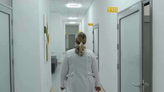 Doctor proceeds through contemporary corridor of healthcare facility. Woman prepares to provide medical care to patient. Slow motion