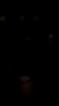 Warm golden and orange bokeh candle lights glow on dark black background. Blurred lights shift and fade gradually, creating romantic abstract ambient atmosphere for holiday celebration.