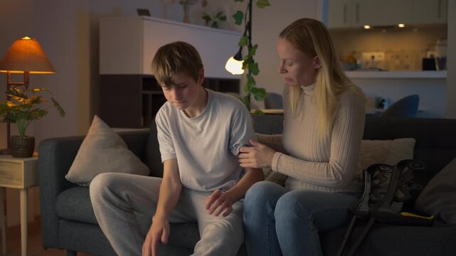 Caring mother supporting her injured teenage son as he uses crutches at home. Family care, emotional support, compassion, injury recovery and rehabilitation concept.