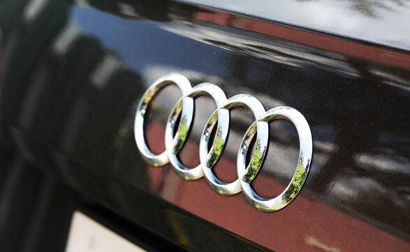 Belarus, Bobruisk 15.07.2026: A metal Audi logo featuring four interlocking rings on the car's dark bodywork. The chrome emblem reflects green foliage and the blue sky, hinting at the setting. 