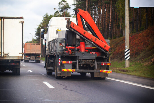 White flatbed truck with red crane arm drives on highway alongside other commercial vehicles, forest line backdrop