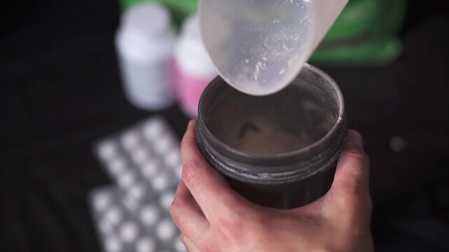 Top view of man finishing pouring gainer powder into fitness shaker
