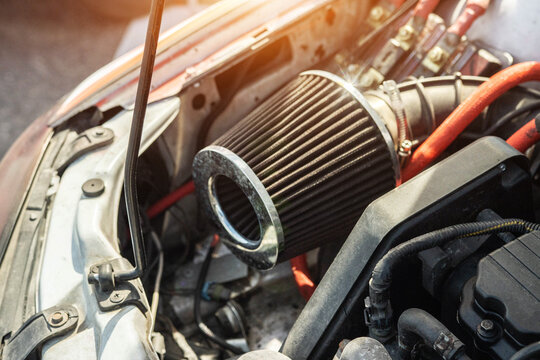 Performance air filter installation in car engine bay. Close-up of aftermarket cone air intake system with red wiring, hood open, detailing automotive tuning and modification.