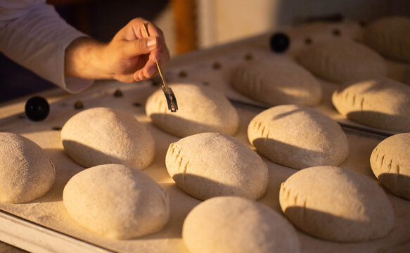 Close up of baker hand scoring bread dough with lame tool preparing numerous loaves for baking process at bread factory production