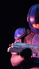 Person in futuristic blue armor holding modern science fiction weapon, intense purple and magenta light on advanced military combat uniform, black background vertical photo © HENADZY
