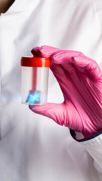 Hand in pink medical glove holding transparent sample container with red cap containing object emitting blue light, vertical photo. Concept of coprogram and analysis for calprotectin with Helicobacter