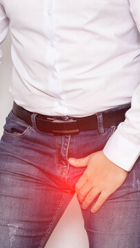 Person clutching groin area with red highlight indicating pain, discomfort, medical symptom of potential urological or reproductive issue, standing indoors, vertical photo, epididymitis