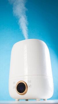 White electric humidifier operating, emitting visible stream of water vapor into air, digital display showing current room temperature and humidity level, modern home appliance, vertical photo