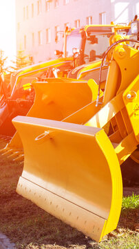 Yellow snow plows and road maintenance vehicles parked outdoors under warm sunlight, showing heavy equipment machinery for winter work or infrastructure projects vertical photo