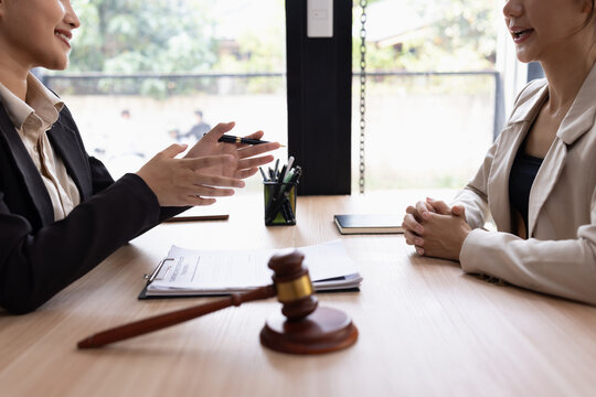 Two professional lawyers sitting at a wooden table discussing documents and legal agreements, with a judge's gavel in the foreground, representing law, consultation, and corporate negotiation.