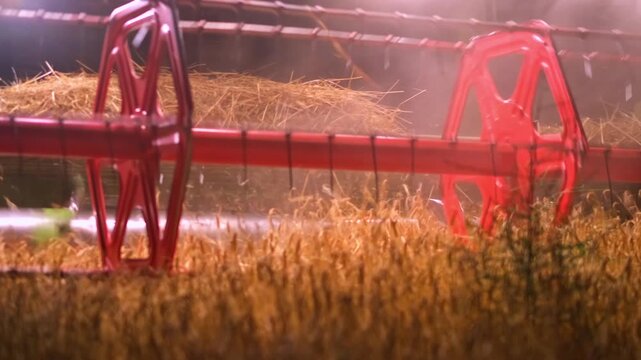 A combine harvester cuts barley at night, moving through a dark field with its red header and bright work lights. Illuminated stubble and rising dust create a dramatic, cinematic remote harvest scene.