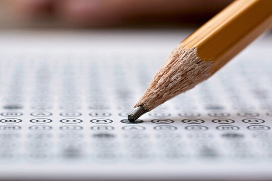 Close-up of sharpened pencil tip poised over multiple-choice bubbles on a test paper, signifying education and assessment