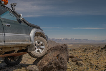 Close up of off-road SUV car tire climbing on huge rock boulder. Overlanding road trip exploration in remote scenic stony mountain wilderness desert landscape at sunny day. © ANDREY