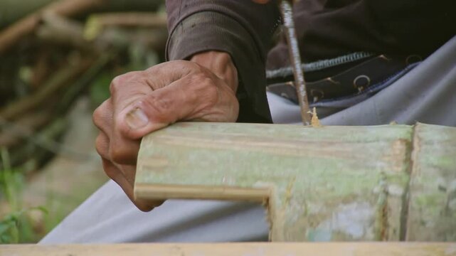 Old hands shape bamboo with care and precision. Nature's materials transformed through skilled, patient hands. Calm, focused movement in a quiet, rustic setting. Perfect for themes of tradition