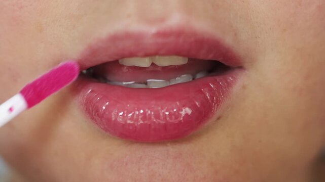 Close-up of woman applying glossy pink lip gloss with applicator