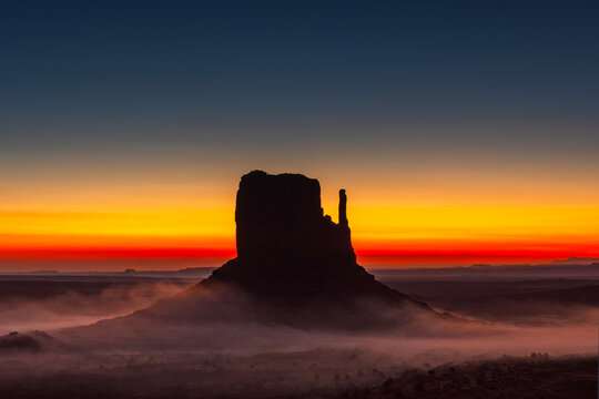 Monument Valley Butte Silhouette at Sunrise with Desert Mist and Vibrant Dawn Sky, Arizona Utah USA