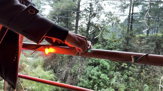 Person installs bulb into glowing string of Christmas lights on outdoor railing, green festive glow
