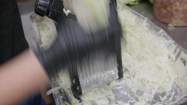 Close up of cook shredding fresh cabbage with a mandoline slicer in a commercial kitchen during food preparation for salads coleslaw and restaurant meal service.