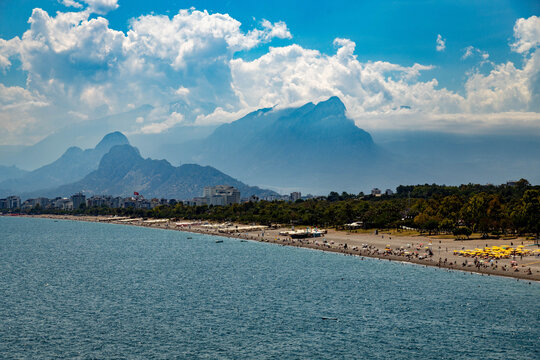 Scenic view of Konyaalti beach and coastline with hazy Taurus mountains in background on sunny summer day in Antalya, Turkey. Popular Mediterranean travel destination with blue sea and clouds.
