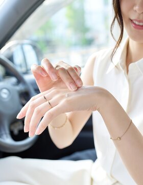 車内で運転前に手の甲へ日焼け止めを塗る若いアジア人女性