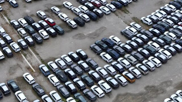 Hundreds of passenger vehicles are parked in organized rows across a large automotive storage yard, highlighting mixed vehicle body styles, inventory management and logistics operations aerial