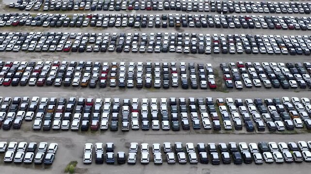 Thousands of passenger vehicles fill an extensive storage yard where organized parking rows, wide service lanes and inventory management illustrate the scale of modern automotive logistics operations.