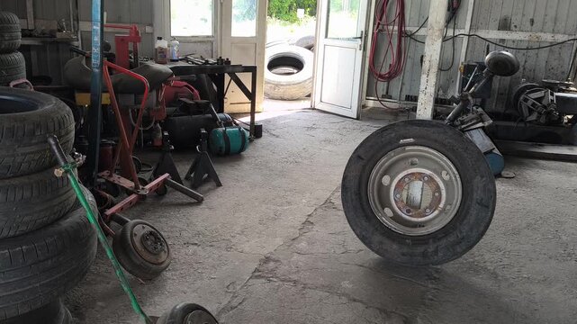 Inside an auto repair shop with tall stacks of used car tires, a red hydraulic jack, and a tire changer. Authentic garage environment perfect for automotive maintenance and auto service concepts.