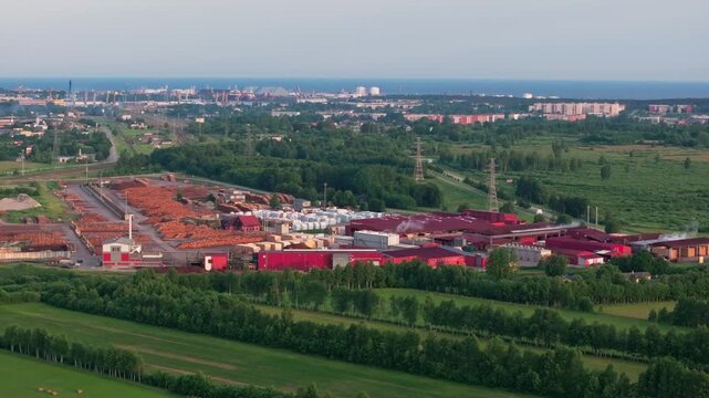 Aerial drone footage of a large timber processing and wood manufacturing facility near Ventspils, Latvia, captured at sunrise. Extensive log storage yards, industrial buildings, railway infrastructure