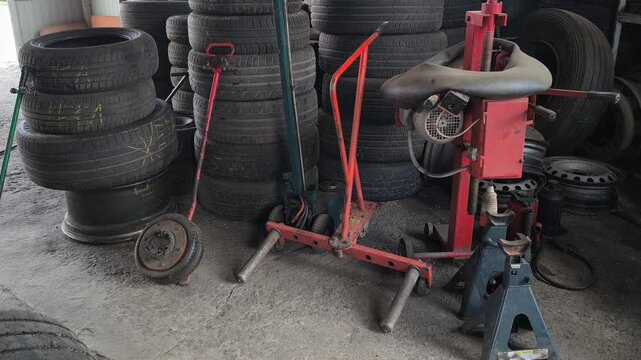 Inside an auto repair shop with tall stacks of used car tires, a red hydraulic jack, and a tire changer. Authentic garage environment perfect for automotive maintenance and auto service concepts.