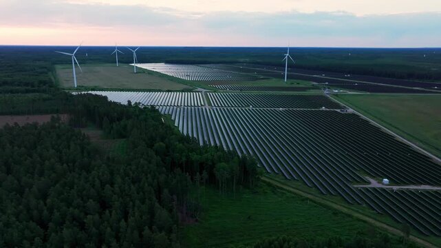 Spectacular aerial drone footage captured at sunrise above one of Latvia's largest renewable energy sites near Pope and Ventspils. Endless rows of photovoltaic solar panels and modern wind turbines.