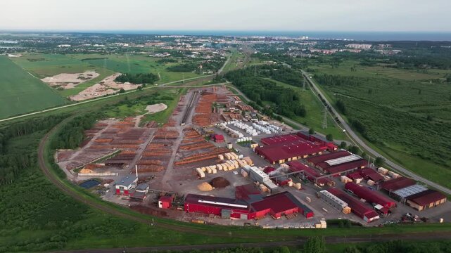 High-quality aerial drone footage of a large timber processing and wood manufacturing facility near Ventspils, Latvia, captured during sunrise. Extensive log storage yards, industrial buildings, railw