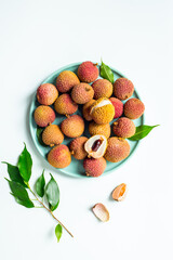 Fresh lychee fruit with green leaves on a plate, top view © 9dreamstudio