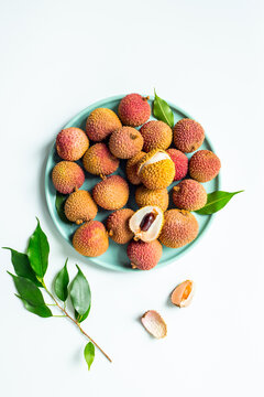 Fresh lychee fruit with green leaves on a plate, top view