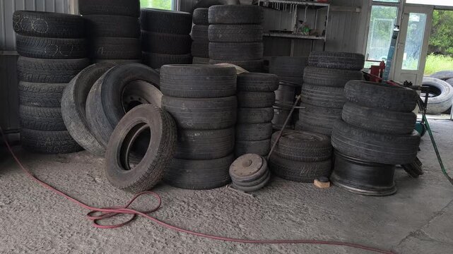 Inside an auto repair shop with tall stacks of used car tires, a red hydraulic jack, and a tire changer. Authentic garage environment perfect for automotive maintenance and auto service concepts.