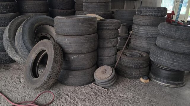Inside an auto repair shop with tall stacks of used car tires, a red hydraulic jack, and a tire changer. Authentic garage environment perfect for automotive maintenance and auto service concepts.