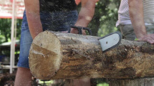 Horishni Plavni, Ukraine-July 15th,2026: Man using chainsaw to cut a large log in an outdoor setting