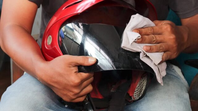Close-up of a man cleaning a motorcycle helmet visor with a microfiber cloth at home before riding, removing dust and smudges as part of routine helmet maintenance.