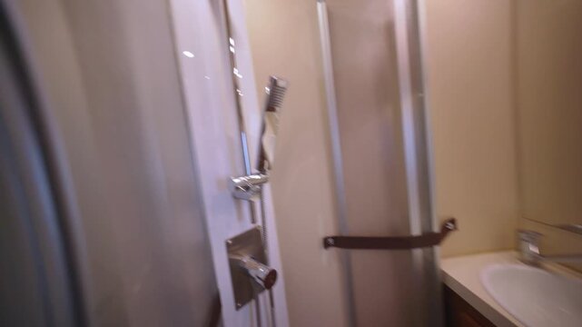 Smooth camera movement showing the interior of a small, functional bathroom inside a recreational vehicle, featuring a toilet, sink, and an enclosed shower with wooden and chrome details