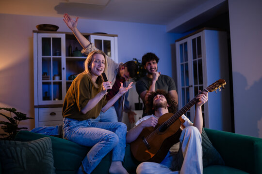 Friends singing karaoke and playing guitar together at home party
