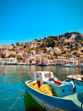Close-up view of Symi Island waterfront, colorful neoclassical houses along the harbor, crystal-clear sea, charming Greek island architecture, sunny Mediterranean day