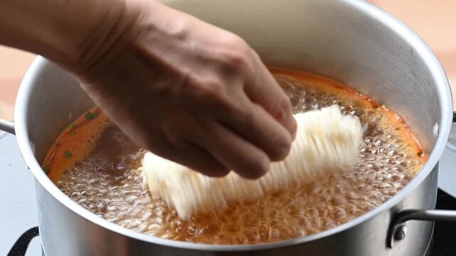 Putting instant noodles into a pot with boiling water to make spicy noodle soup