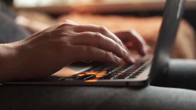 Close-up of hands typing on a laptop keyboard with warm backlighting