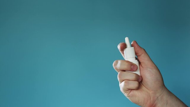 Hand holding a white nasal spray bottle against a blue background