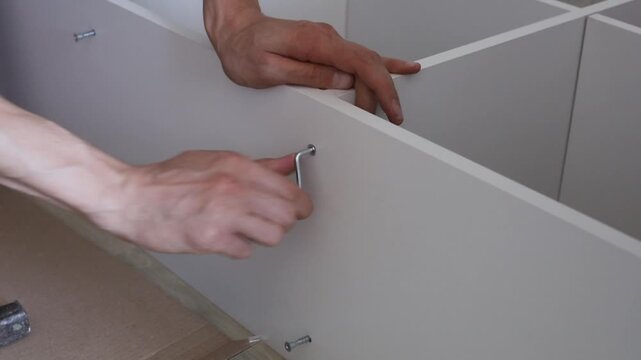 Hands assembling furniture with screws and tools in a well-lit indoor setting