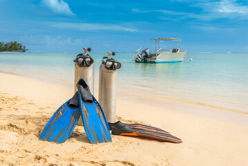 Scuba diving gear on display at pristine tropical beach diving holiday destination of Moorea, French Polynesia, with diving boat in the background, dive tank and masks, on sunny day with blue skies © lupiphoto