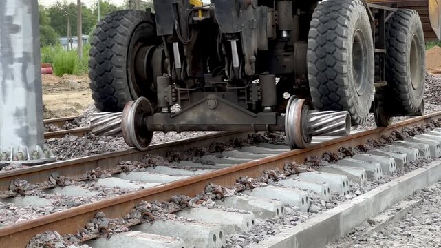 A hi-rail excavator with flanged steel wheels moving along railway tracks outdoors. Railway transport, track maintenance, heavy machinery.