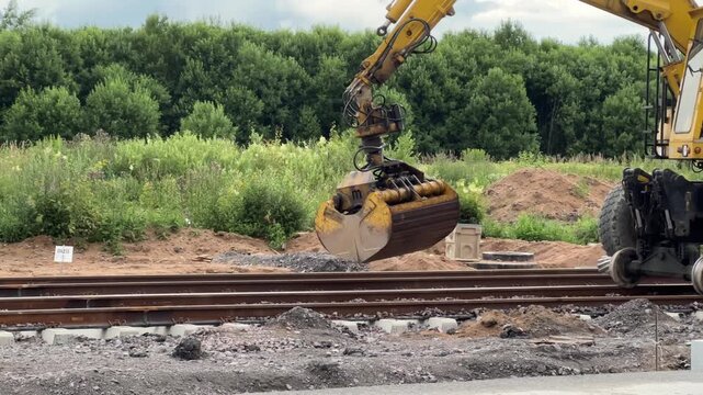 A hi-rail excavator operating a bucket on a railway construction site outdoors. Railway construction, track maintenance, heavy machinery.