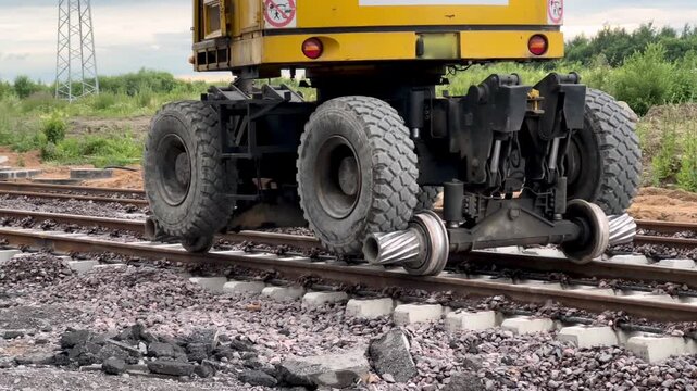 A hi-rail excavator with special steel wheels driving on railway tracks. Railway transport, track maintenance, heavy machinery.